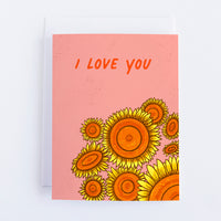 A pink greeting card with 9 sunflowers in the bottom right quadrant and I Love You in the top half of the card.