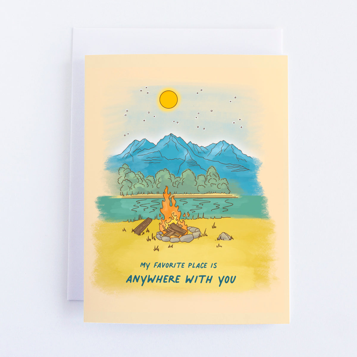 A greeting card with a campfire in a fire ring burning in a little field next to a lake with a forest and mountains in the background. With a beige background.
