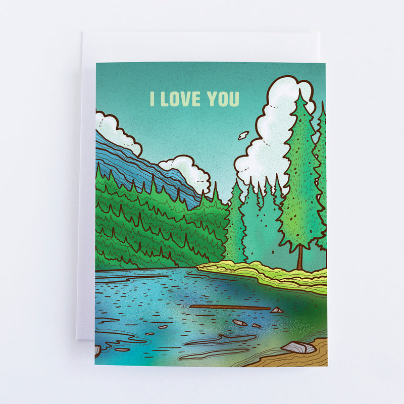A greeting card with a blue lake and trees and mountains in the background the sky is blue and the text says I love you