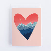 A light pink card with a dark pink hear that has three rows of blue mountains at the bottom of the heart and a row of trees. In the top left of the heart is a crescent moon. 