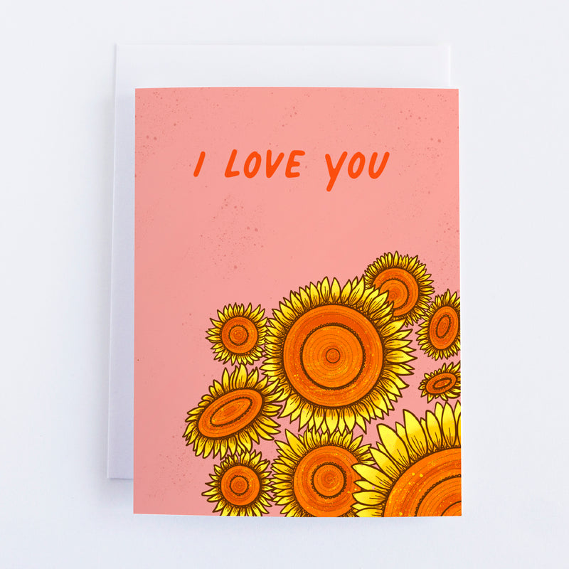 A pink greeting card with 9 sunflowers in the bottom right quadrant and I Love You in the top half of the card.