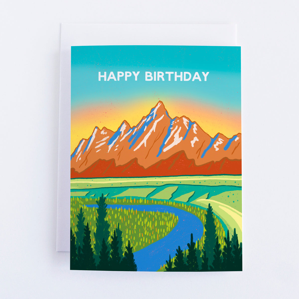 A card with the teton mountains and a blue pink and yellow sky with a river and trees in the foreground. The text says happy birthday in the sky.